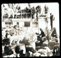 Image of Inuit, dogs, barrels; other men watch